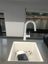 Modern white kitchen sink and pull-down faucet in an RV rental, with a view of greenery outside.