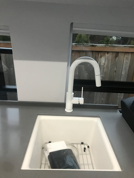 Modern white kitchen sink and pull-down faucet in an RV rental, with a view of greenery outside.