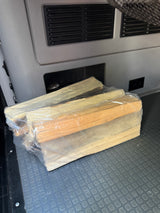 Bundled firewood, wrapped in plastic, rests on a textured floor mat in an RV rental interior, ready for a camping trip.