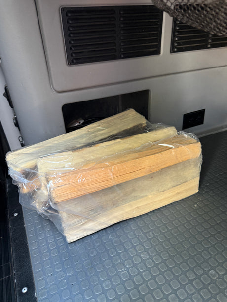 Bundled firewood, wrapped in plastic, rests on a textured floor mat in an RV rental interior, ready for a camping trip.