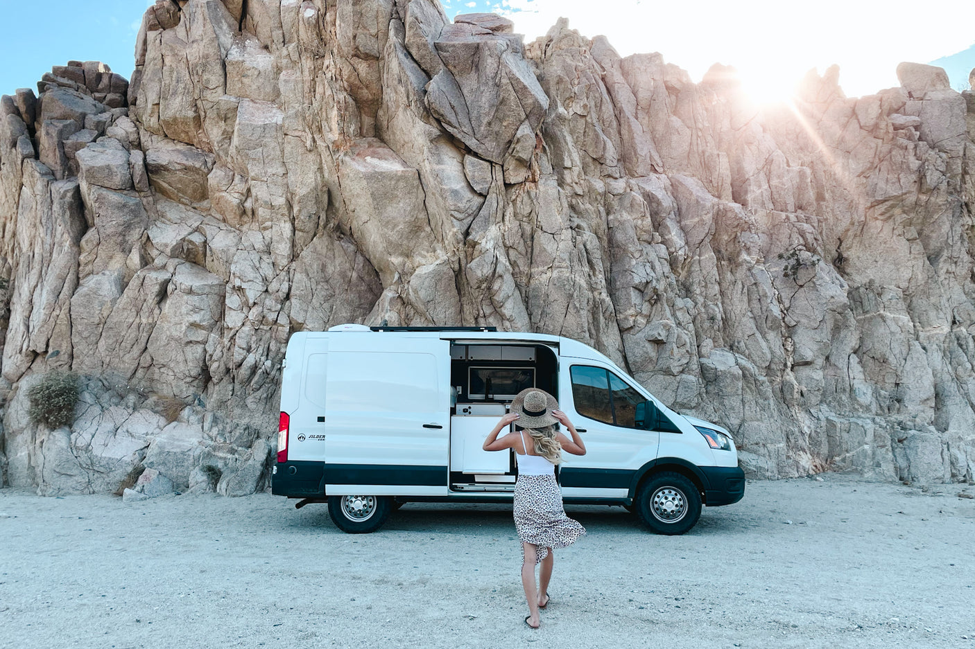 Van life adventure: A white rv rental parked by huge desert rocks. Person approaches open side.