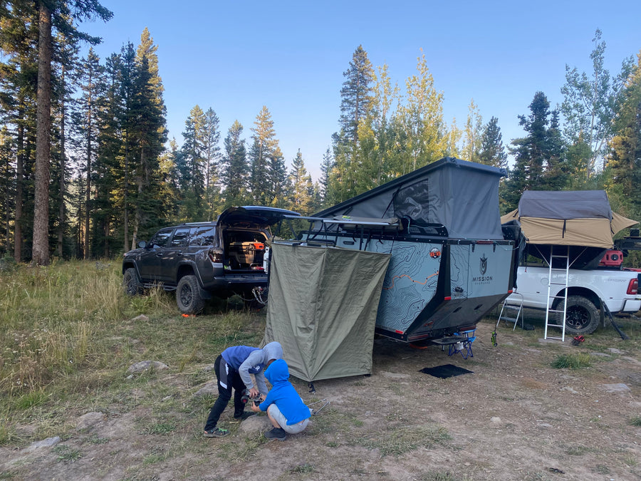 Campsite in a forest with an SUV, teardrop trailer, and truck with rooftop tent. Great for an RV rental adventure as kids play.