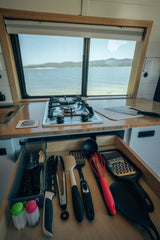 RV rental kitchen with a scenic lake view: built-in stove, counter, and a drawer stocked with cooking utensils.