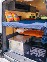 Spacious RV rental interior featuring two bunk beds with colorful pillows, overhead storage, and an aluminum gear box.
