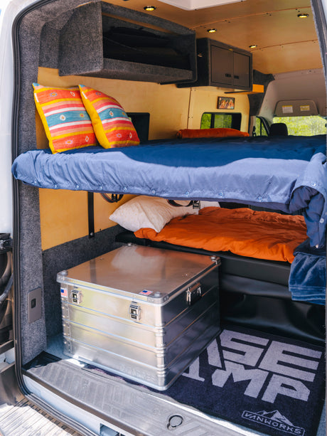 Spacious RV rental interior featuring two bunk beds with colorful pillows, overhead storage, and an aluminum gear box.