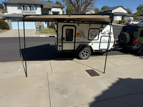 A compact Forest River No Boundaries RV rental with an extended Rhino-Rack awning, hitched to a Jeep, parked on a driveway.