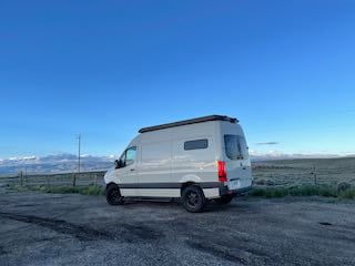 White camper van **RV rental** parked outdoors with mountains & blue sky. Perfect for your next road trip adventure.