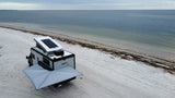 An RV rental, complete with a solar-paneled pop-top and extended awning, offers serene beach camping by the ocean.