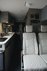 Explore this modern rv rental interior, featuring bright quilted seats, a compact kitchen, and overhead control panel.