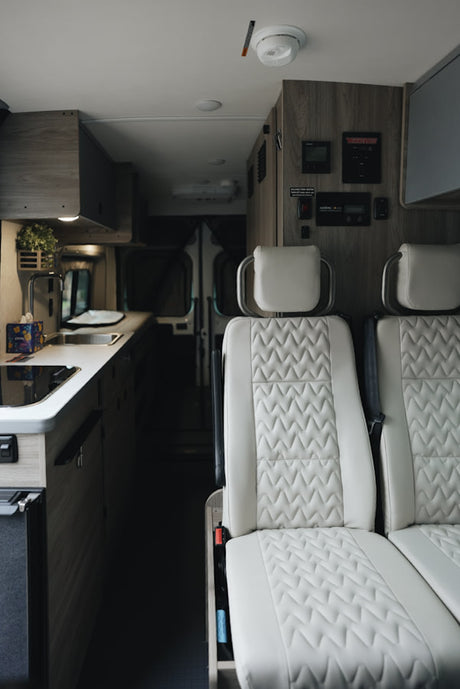 Explore this modern rv rental interior, featuring bright quilted seats, a compact kitchen, and overhead control panel.