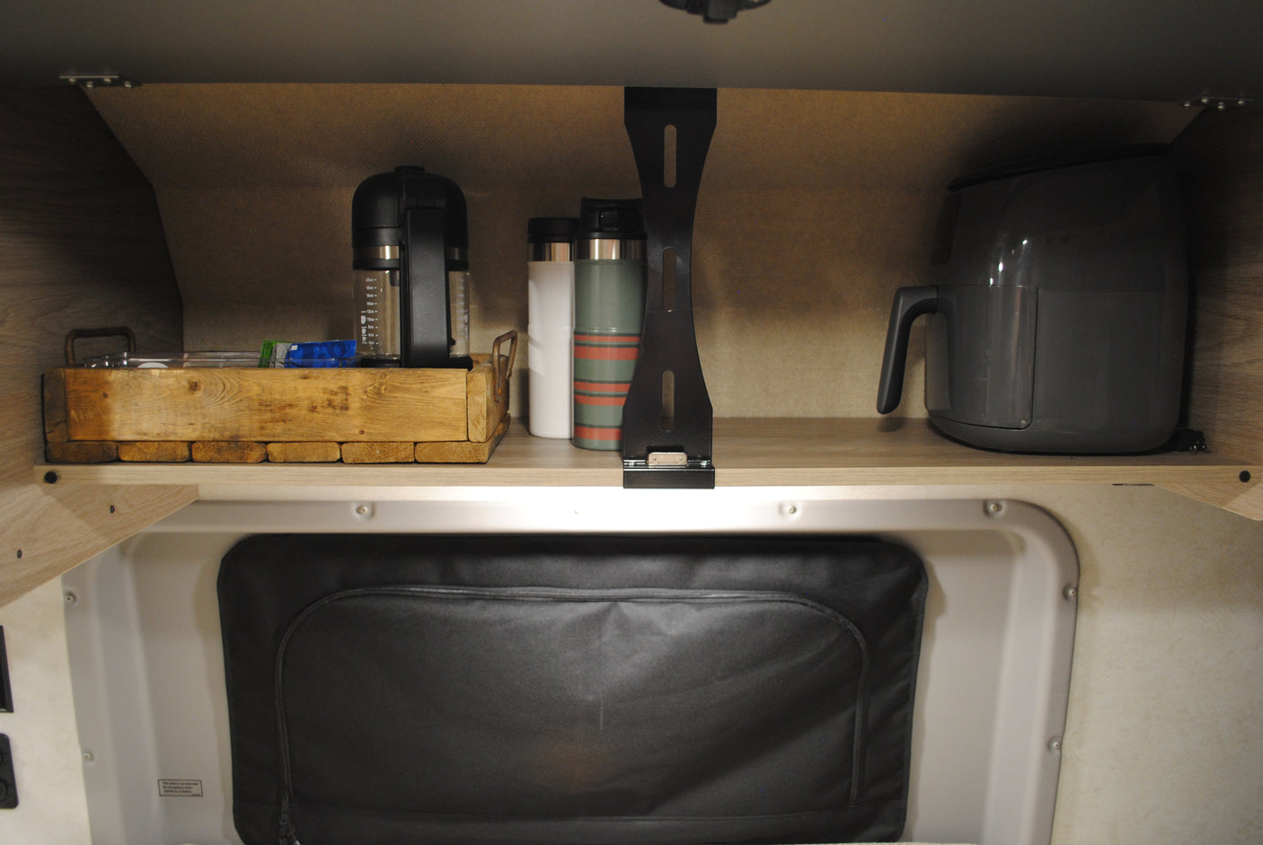 RV rental interior: A compact shelf holds a coffee maker, an air fryer, and travel mugs, neatly organized for mobile living.