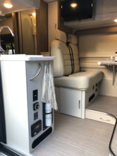 Clean RV rental interior: Bright mobile living space with control panel, cream seating, dining area, and wall-mounted TV. — photo 15