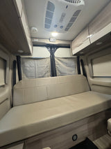 Spacious RV rental interior featuring a comfortable light-colored bench seat/bed, overhead cabinets, and ceiling AC unit.