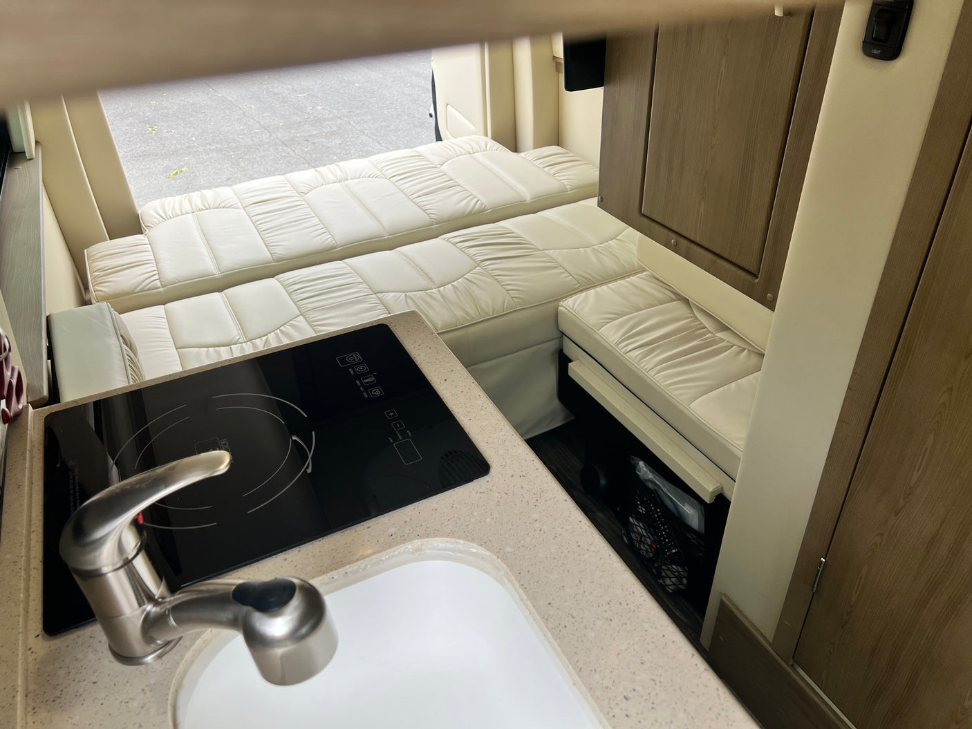 Inside an RV rental: a compact kitchen with sink and induction cooktop, leading to convertible sleeping areas.
