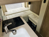 Inside an RV rental: a compact kitchen with sink and induction cooktop, leading to convertible sleeping areas.