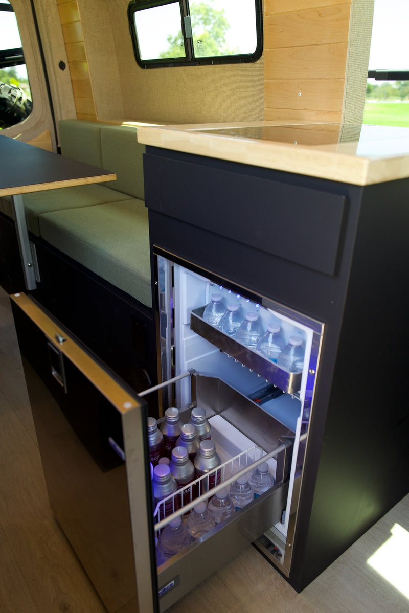 Modern rv rental: pull-out fridge with blue LED lights, stocked drinks, light wood counter, and plush green seating. — photo 18