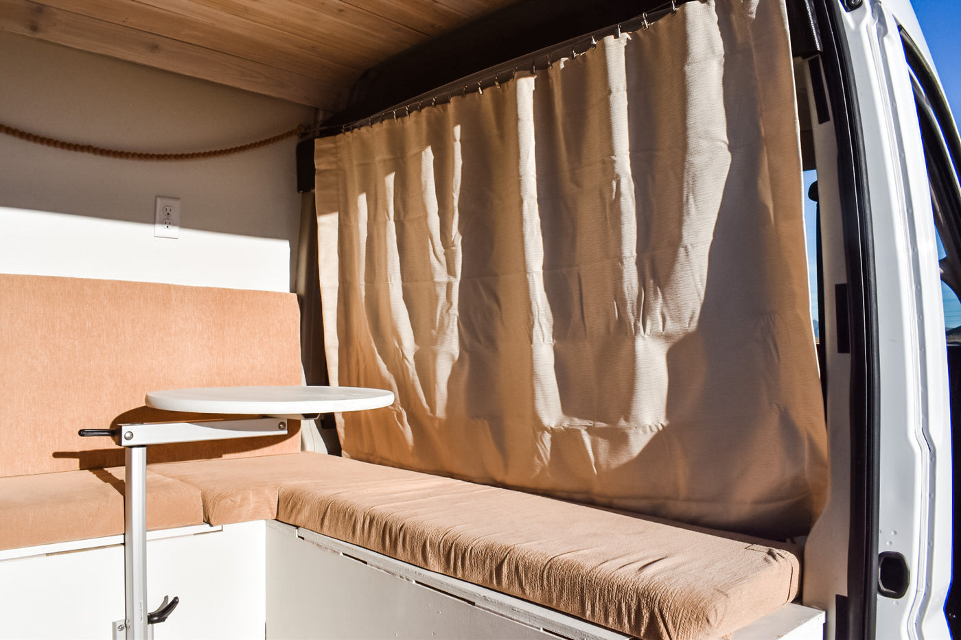 Inside an RV rental: a cozy living space with tan bench seating, a white adjustable table, and a light privacy curtain. — photo 8
