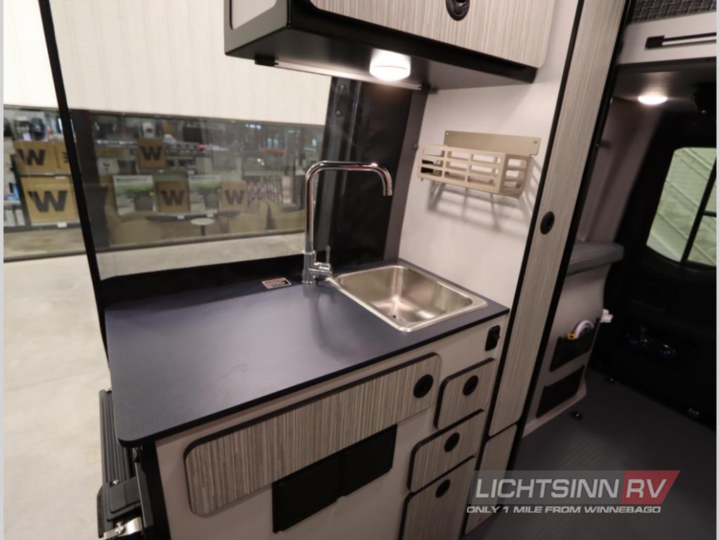 RV rental interior: A compact kitchen with stainless steel sink, chrome faucet, dark countertop, and storage.