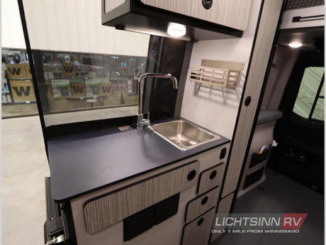 RV rental interior: A compact kitchen with stainless steel sink, chrome faucet, dark countertop, and storage.