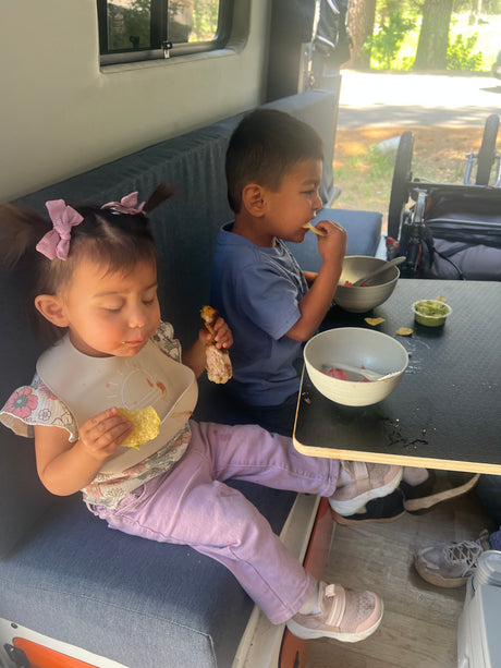 RV rental: Two kids eating chips, chicken, & fruit inside. Perfect family adventure meal.