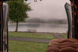 Misty lake view from an RV rental, featuring a tree, picnic table, and scenic path. A cozy campervan retreat.