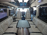 Luxury rv rental interior: light grey quilted seating, central table, and large TV. A spacious, comfortable mobile living space.