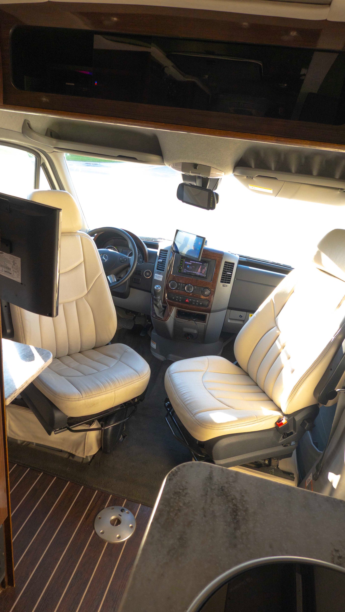RV rental cab: cream leather seats, Mercedes dashboard, entertainment monitor, and wood overhead storage.