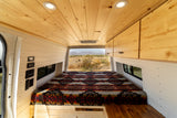 Experience van life: This rv rental shows a cozy camper interior with wooden ceiling, comfortable bed, and a stunning desert view.