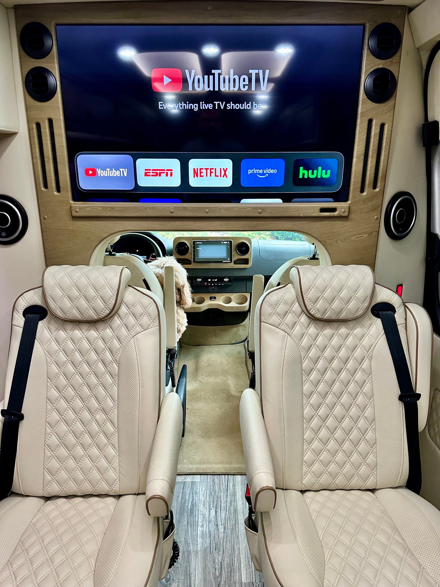 Luxurious rv rental interior featuring quilted cream seats and a TV displaying YouTube TV, ESPN, Netflix, Prime Video, and Hulu.