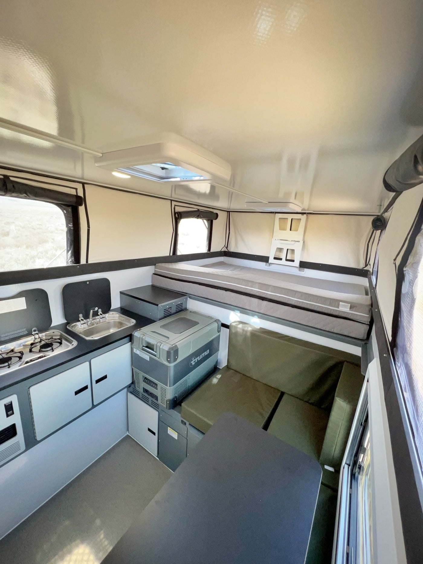 This RV rental's spacious pop-up interior features a kitchen with stove/sink, a portable fridge, a bed, and a dining/lounge area. — photo 7