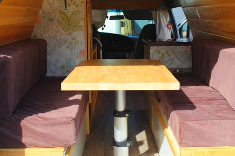 RV rental's inviting interior: light wood dining table between cushioned benches. Note the botanical wallpaper & front cab view.