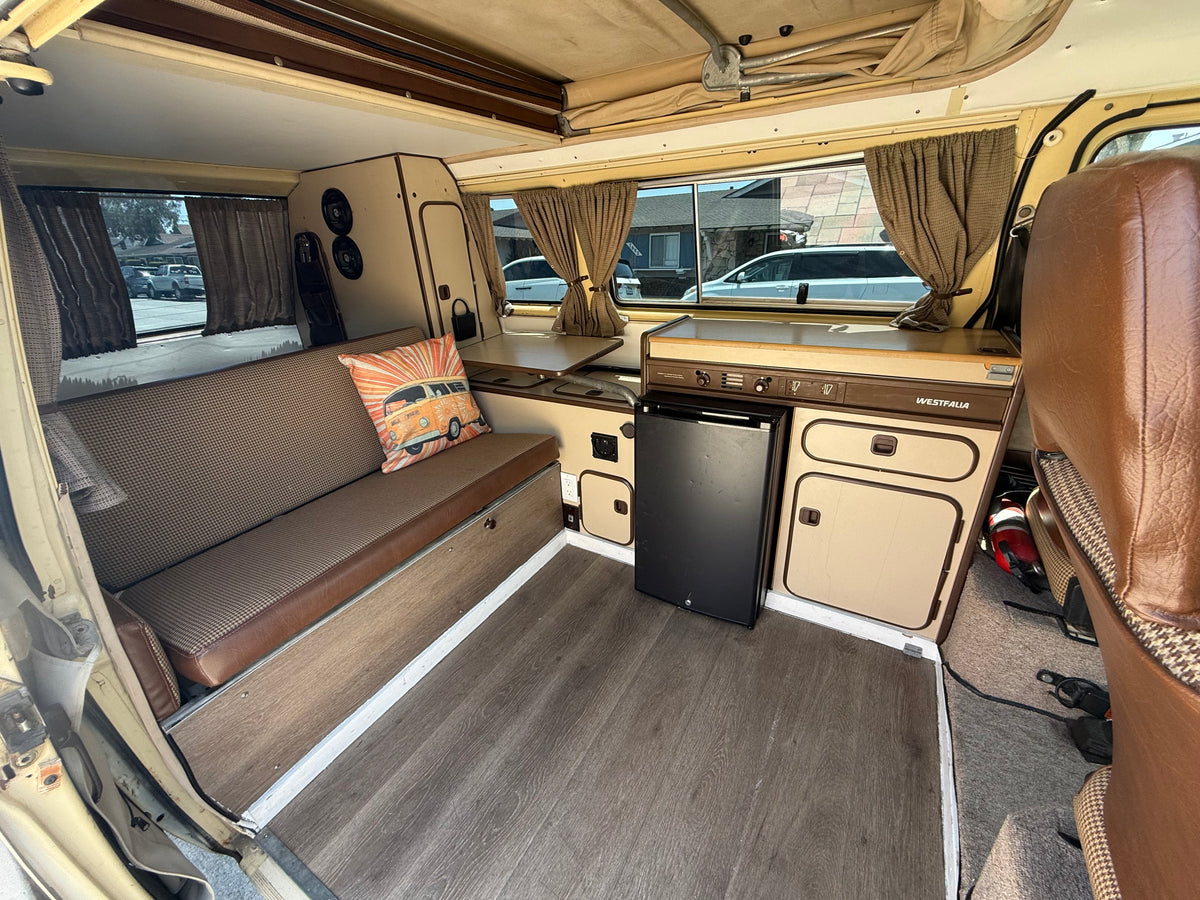 Cozy vintage VW Westfalia camper van rv rental interior, featuring kitchenette, patterned bench seating, and pop-top roof.