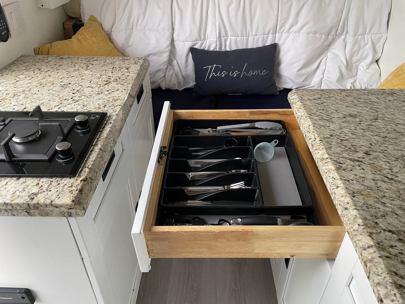 Compact RV rental kitchen with pull-out cutlery drawer, stovetop, and cozy bed area, showcasing efficient space.