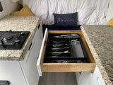 Compact RV rental kitchen with pull-out cutlery drawer, stovetop, and cozy bed area, showcasing efficient space.