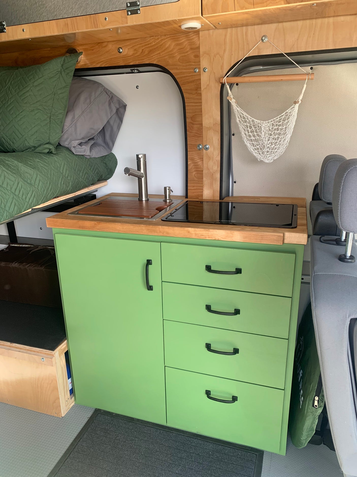 Inside an RV rental: Efficient kitchen setup with green cabinets, sink, and bed area.