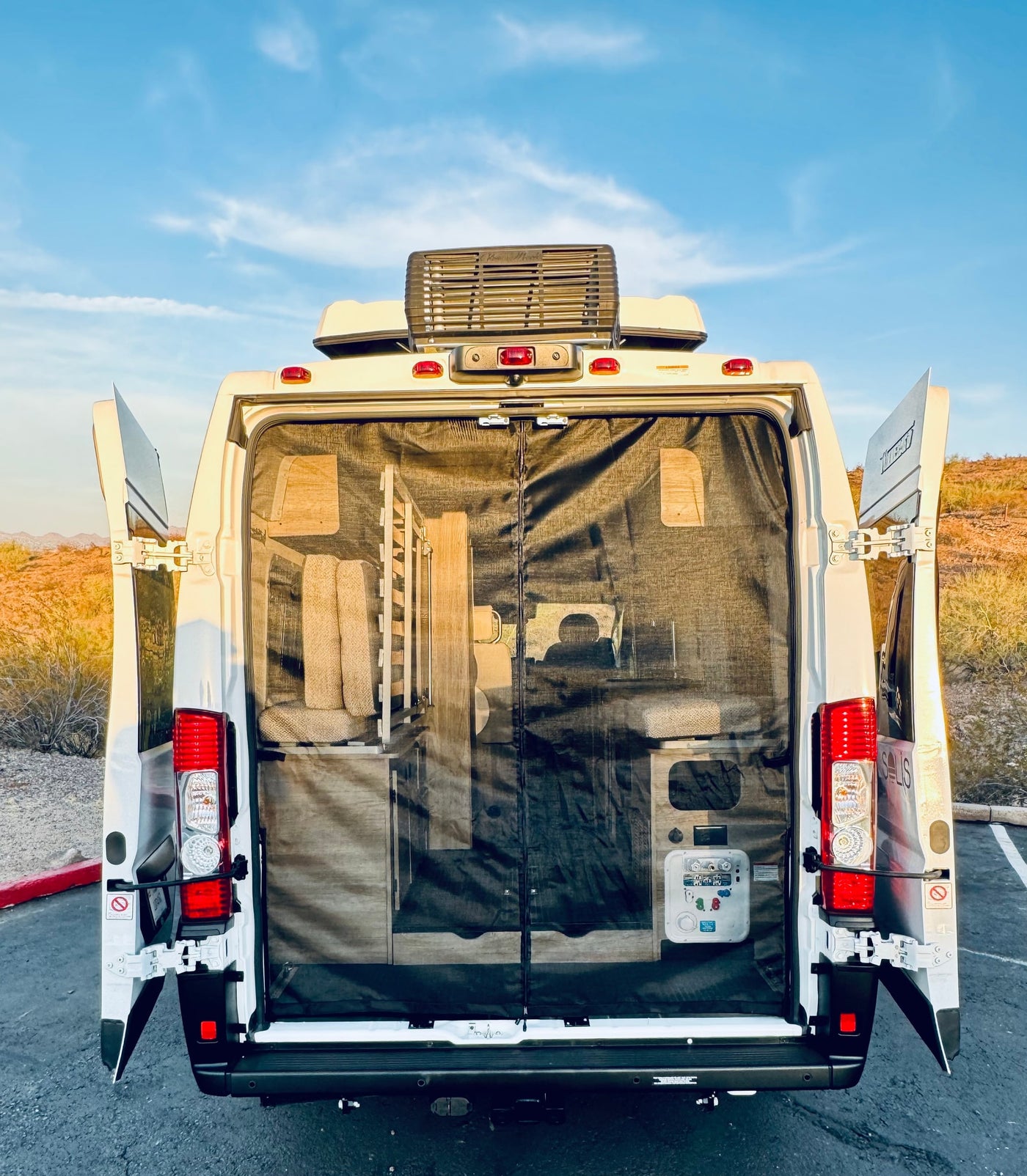  with chairs & an outdoor rug.|A couple and dog relax outside their white Winnebago Solis RV rental in a serene forest setting.|Rear of an RV rental camper van with open doors — photo 9