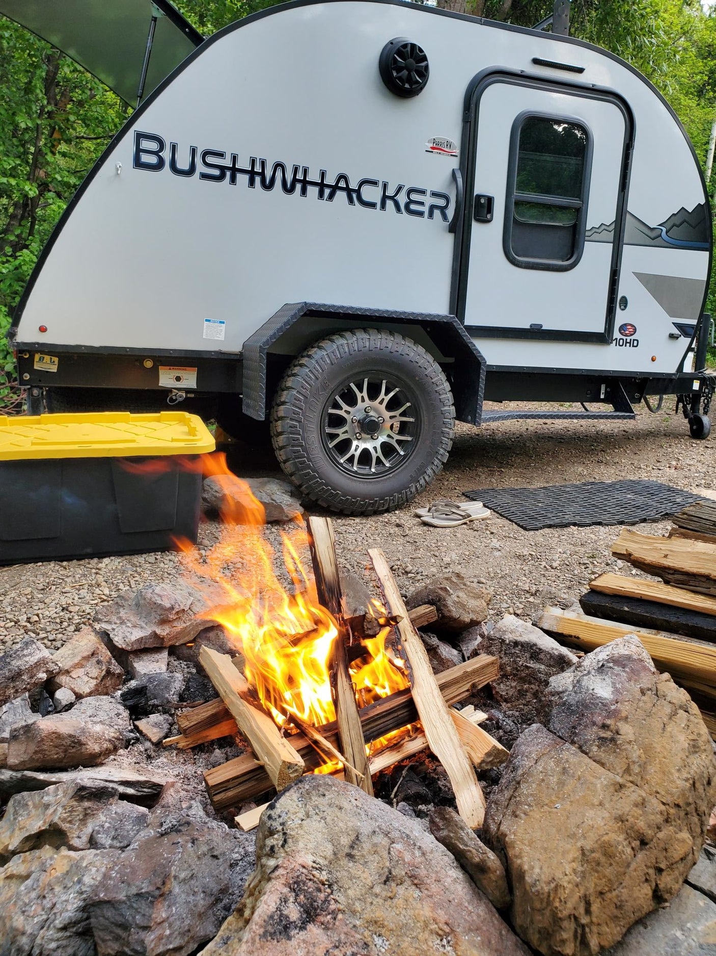 RV rental campsite with a crackling fire and Bushwhacker trailer, perfect for outdoor adventures.