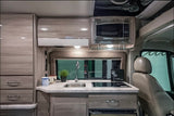 This RV rental showcases a compact, well-appointed kitchen with light wood cabinets, sink, induction cooktop, & microwave. Perfect for mobile living.