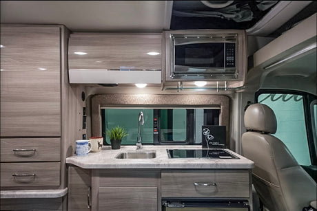 This RV rental showcases a compact, well-appointed kitchen with light wood cabinets, sink, induction cooktop, & microwave. Perfect for mobile living.