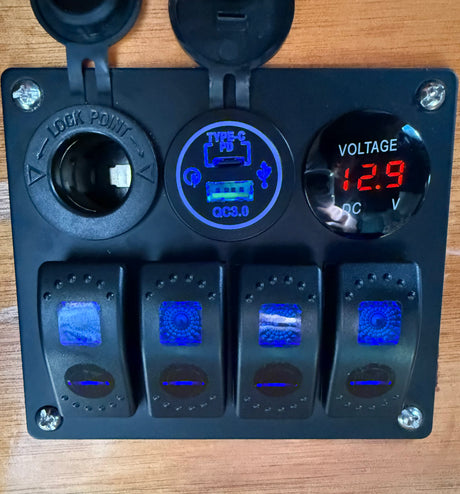 RV rental's black power panel: 12V socket, USB-C PD/QC3.0 charger, red 12.9V voltmeter, and four blue-lit rocker switches.