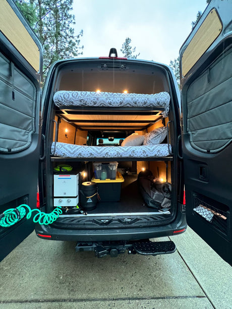 Inside an **RV rental** campervan, rear view: cozy bunk beds, portable water heater, and organized storage for mobile adventures.