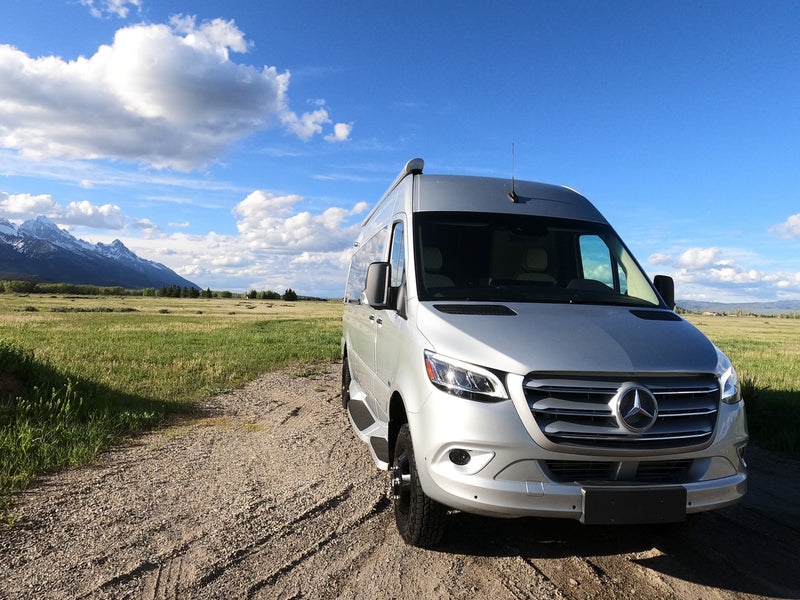 A silver Mercedes Sprinter RV rental van on a scenic gravel road, with snow-capped mountains & blue sky. Ideal for adventure. — photo 3