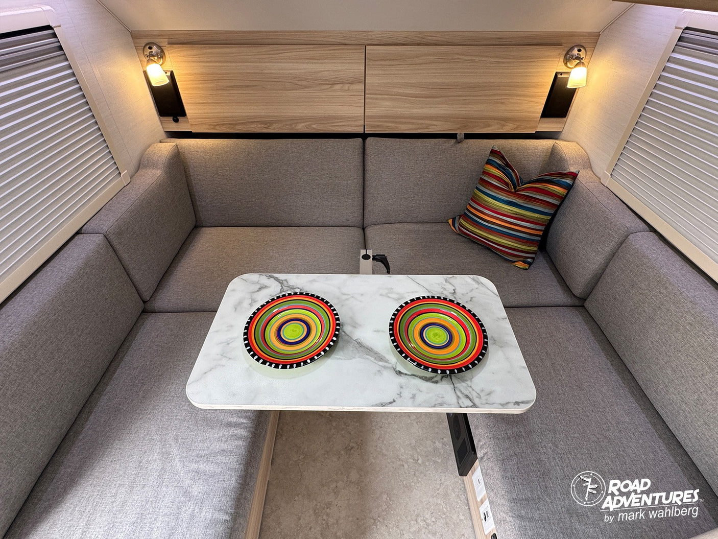 Cozy rv rental interior: U-shaped dinette, stylish marble table with colorful bowls, gray cushions, and warm lighting.