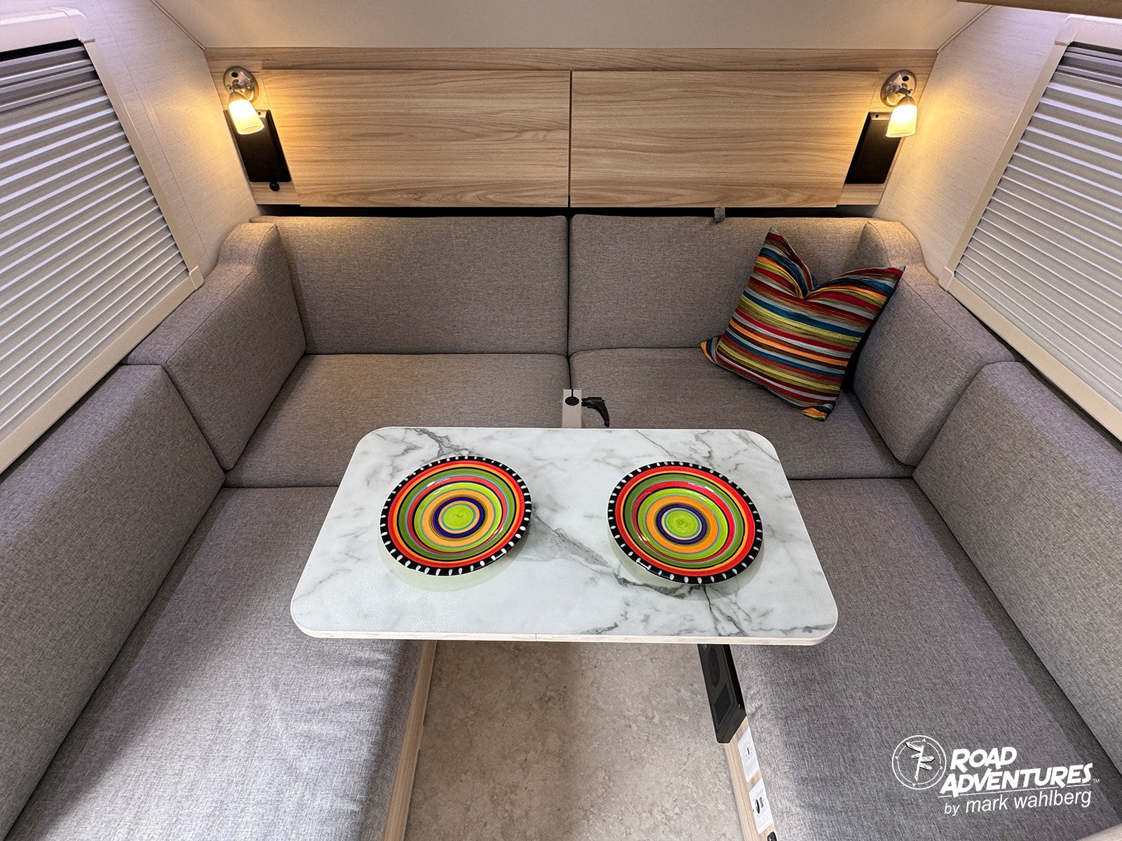 Cozy rv rental interior: U-shaped dinette, stylish marble table with colorful bowls, gray cushions, and warm lighting.
