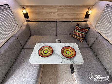 Cozy rv rental interior: U-shaped dinette, stylish marble table with colorful bowls, gray cushions, and warm lighting.