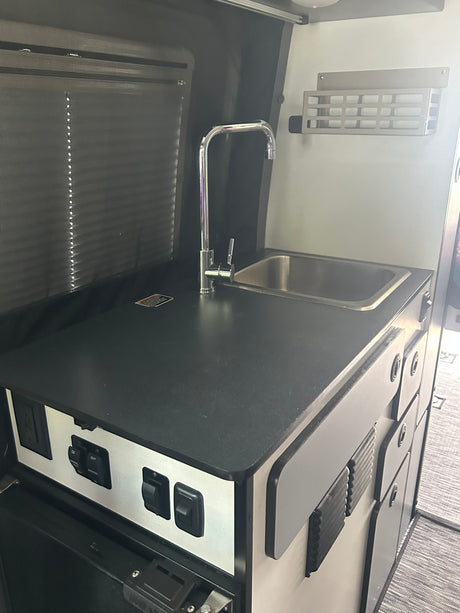 Explore this RV rental's compact kitchenette: stainless steel sink, chrome faucet, and integrated controls. Perfect for on-the-go living.