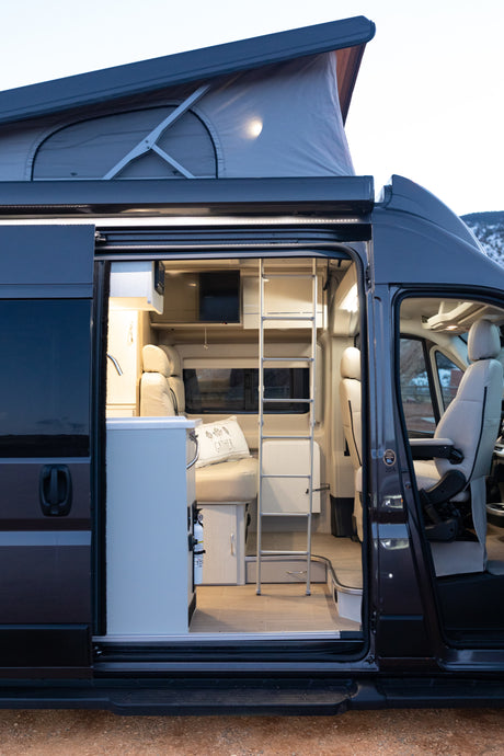 Explore this RV rental's inviting pop-top camper van interior: bright kitchen, cozy seating, and ladder to the upper bed.