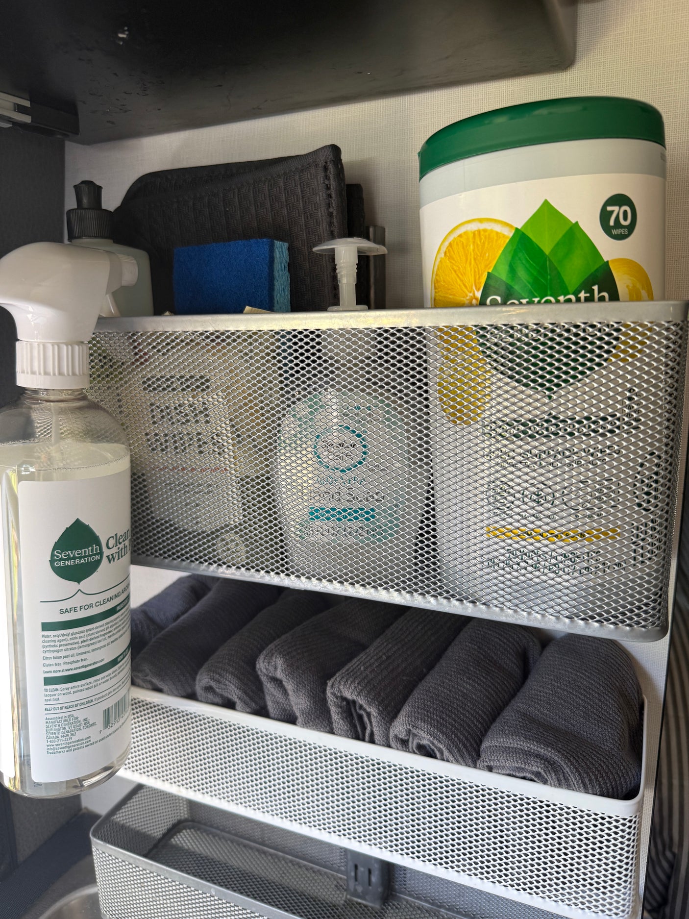 RV rental cleaning essentials: Seventh Generation products, sponge, and rolled towels neatly stored in a multi-tier mesh organizer.