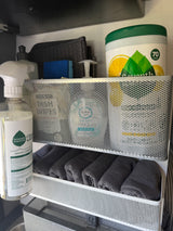 RV rental cleaning essentials: Seventh Generation products, sponge, and rolled towels neatly stored in a multi-tier mesh organizer.