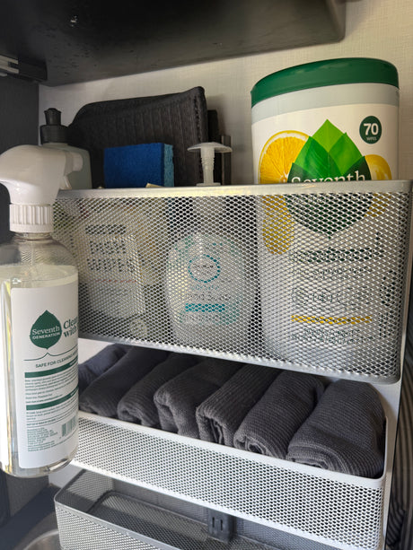 RV rental cleaning essentials: Seventh Generation products, sponge, and rolled towels neatly stored in a multi-tier mesh organizer.